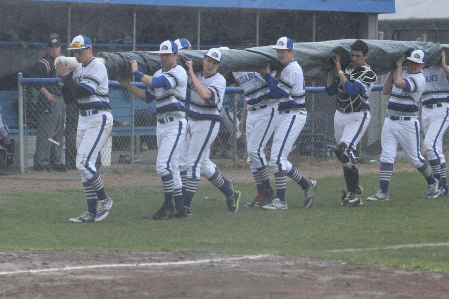 The Lake Central boys baseball team roll out the tarp as the rain begins to come down. They quickly huddled under the dugout to take cover shortly afterwards. 
