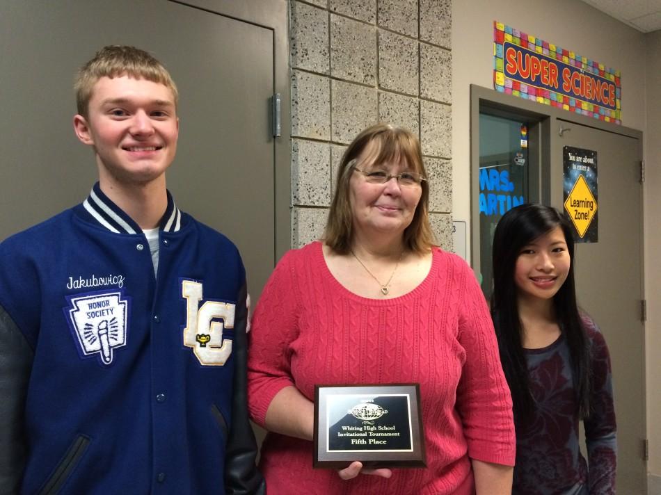 Jake Jakubowicz (12), Mrs. Mary Joan Martin, Science and Anna Hallowell (10) stand in front of Mrs. Martin’s room with the plaque that Science Olympiad won last Saturday, December 6, 2014. Jakubowicz is one of the students who made the schedule, and Hallowell was one of the many students who participated in the competition.