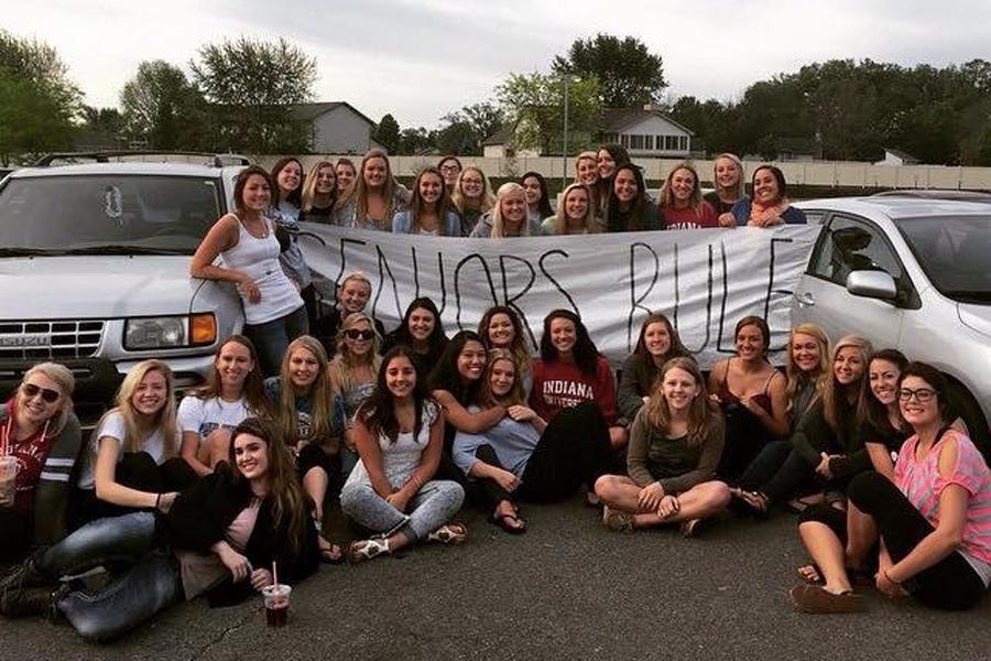 A few of the senior girls gather around a “SENIORS RULE” sign for a picture. The sign, made by Jennifer Mohamed (12),  was hung between two car doors because the students could not find duct tape.