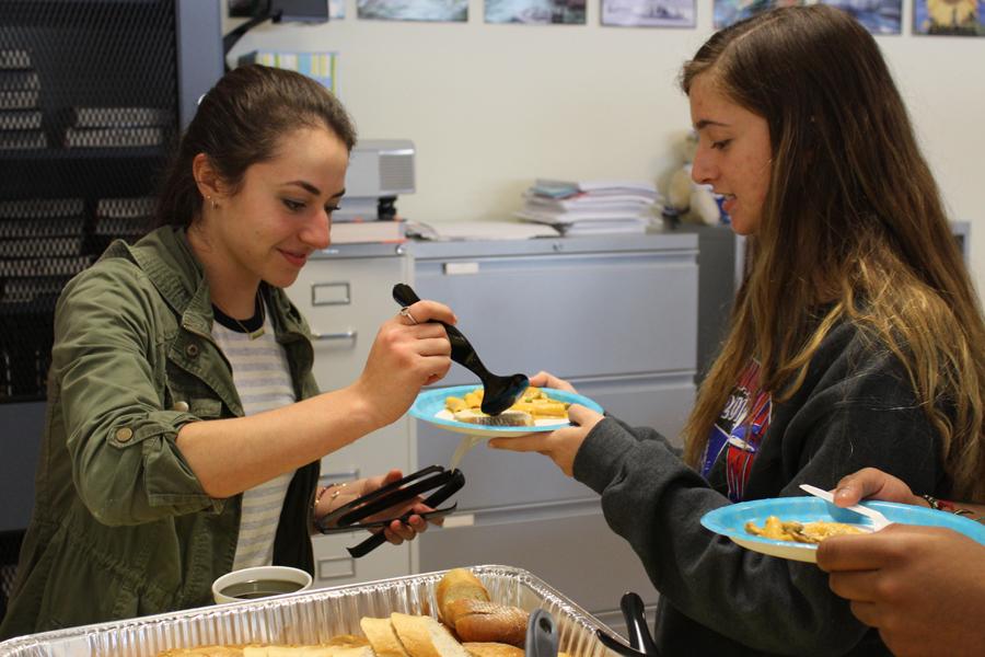 Rachel Gross (12) helps Lauren Granskog (12) place food on her plate. Ciao Bella was served at the International Club meeting on Nov. 3.
