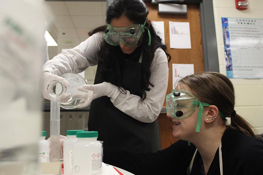 Helena Zakher (11) pours 50 mL of six moles of sodium hydroxide while Rachel Streck (11)  watches. Zakher and Streck were lab partners since the beginning of the year.