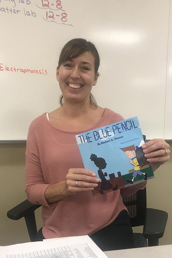 Mrs. Thomas, Science, holds the book she wrote. It is called “The Blue Pencil.”

