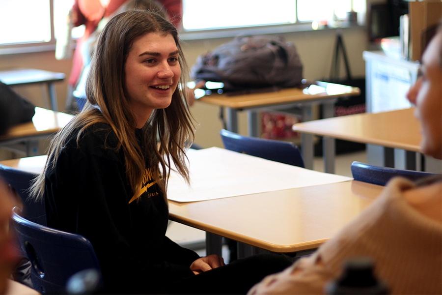 Claire Karberg (12) smiles as she talks to friends at the International Club callout meeting. The room was packed with students learning about other cultures. 
