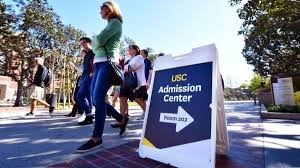 Parents walk past the University of Southern California’s admissions board.  The parents, with students, were touring the school after the incident.