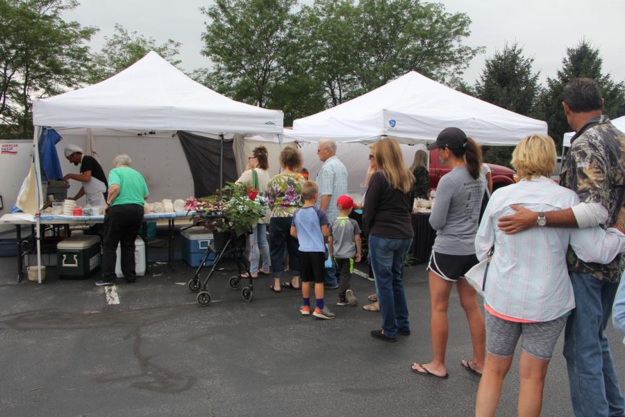 A long line of people wait to choose from the variety of cheeses that are sold at the deli booth. The man worked hard on selling his items.