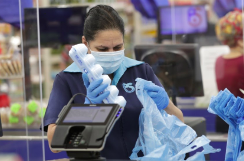 An essential worker at a store carefully bags groceries for a customer. Most workers are required to wear masks and gloves when at work to help stop the spread of the virus.