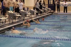 Gripping the block, Kajus Rudzevivius (10) grins widely as he looks at the scoreboard. He achieved 1st place in the 100 Freestyle event.